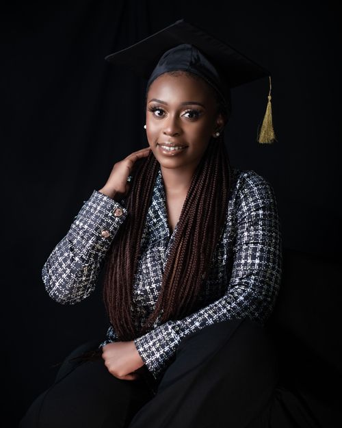Free Portrait of an African American woman graduate smiling with a mortarboard on a dark background. Stock Photo