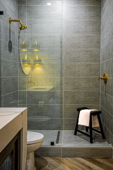Stylish bathroom featuring a glass shower enclosure, stool with towel, and modern fixtures.