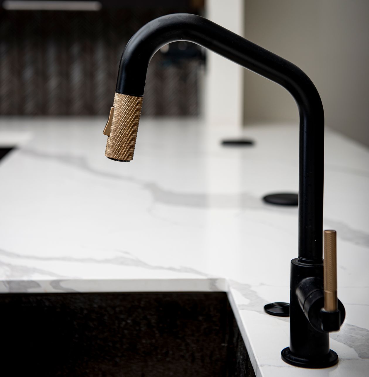 Close-up of a matte black kitchen faucet with a knurled brass spout and handle