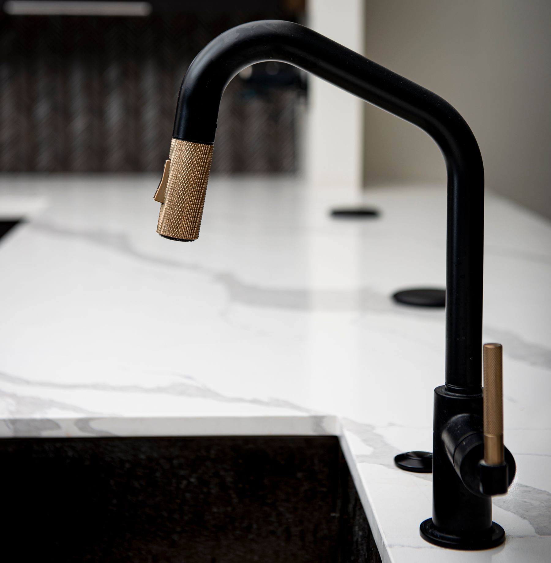 Black tap with a warm metal accent above a white sink and pale worktop