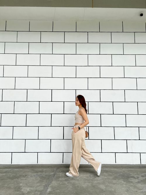 Free A fashionable Asian woman in casual attire walks alongside a white brick wall, exuding modern style. Stock Photo