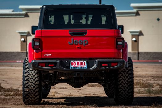 Rear view of a red Jeep SUV parked outdoors with 'No Bull' license plate, showcasing rugged wheels.