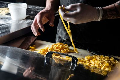 Hands cutting fresh ribbons of pasta on a bench — photo by Derwin Edwards on Pexels