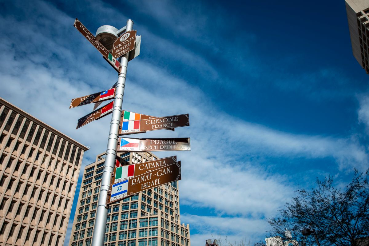 A signpost listing city names and directions with office buildings in the background