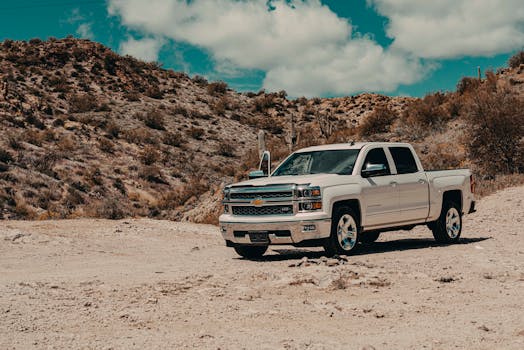 A white pickup truck parked in a scenic desert landscape with arid hills.
