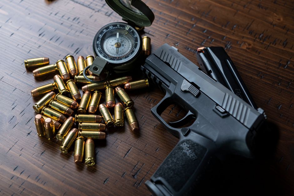 Fotomural Toma en ángulo alto de una pistola, balas y una brújula descansando sobre una superficie de madera.