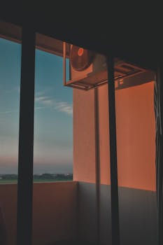 A serene view of a city backdrop from a residential balcony during sunrise, featuring an air conditioner unit.