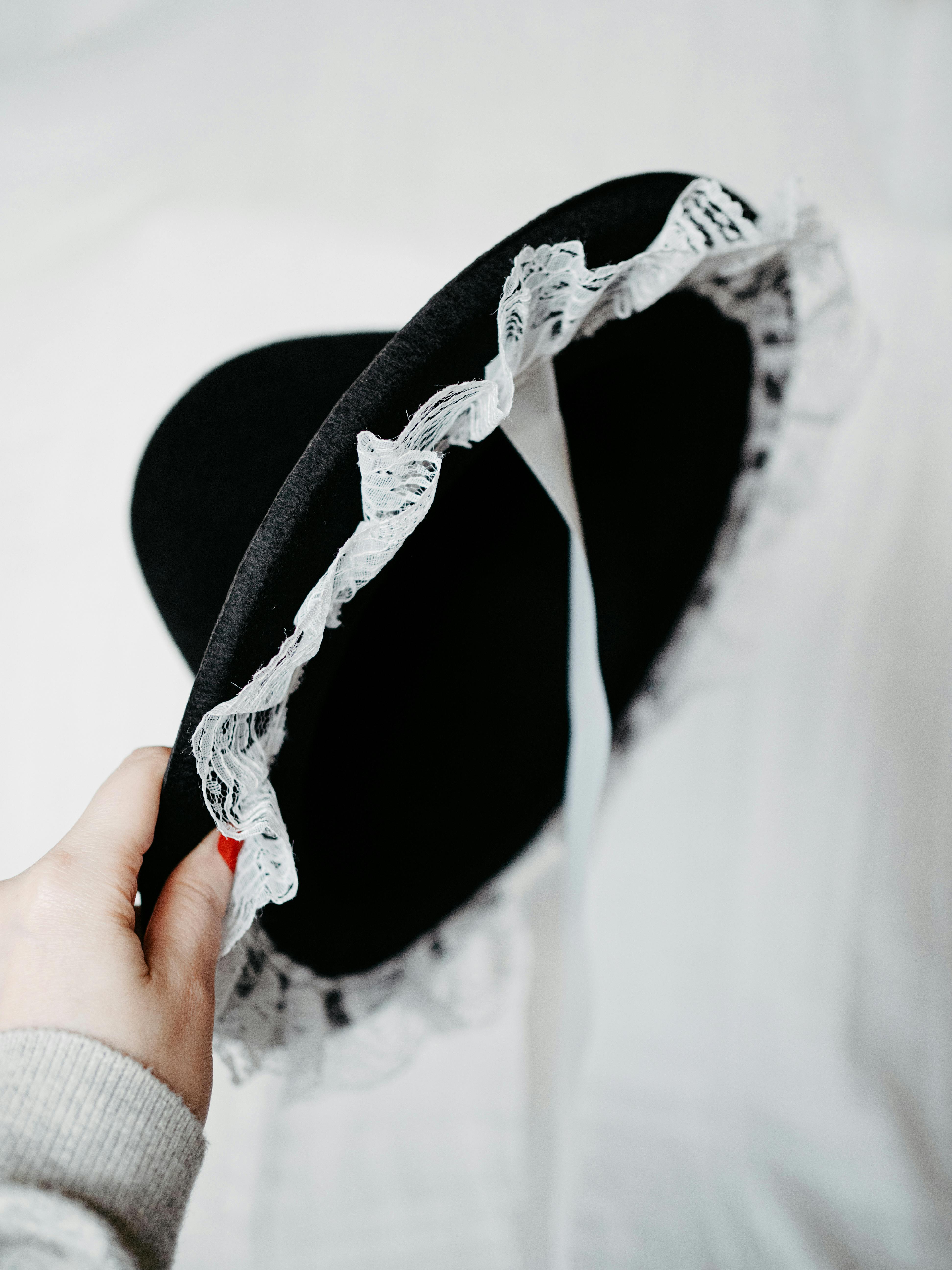Close-up of a hand holding a black hat with white lace, isolated on a white background.