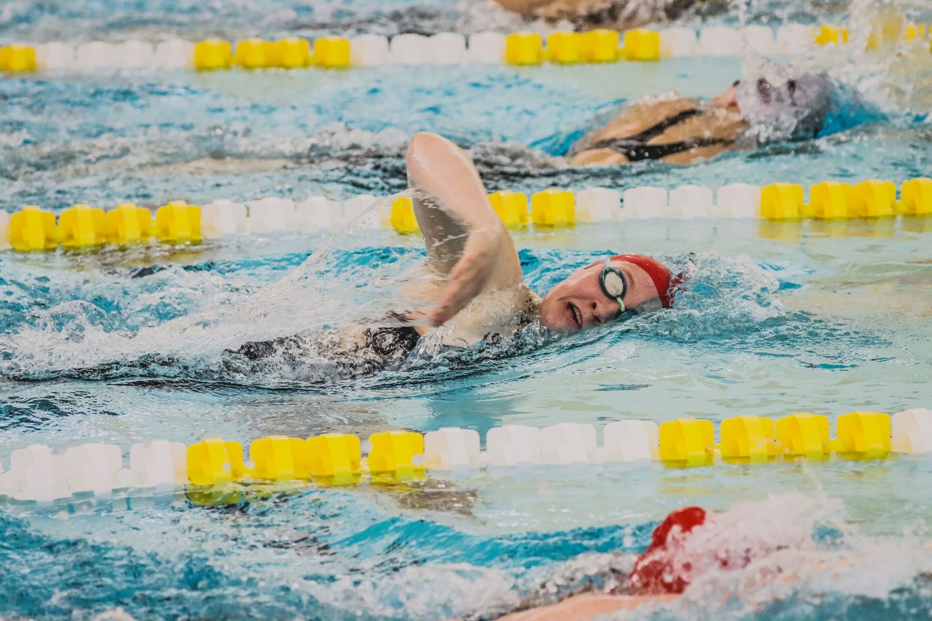 Diverse group of female swimmers racing in a competitive indoor pool event.