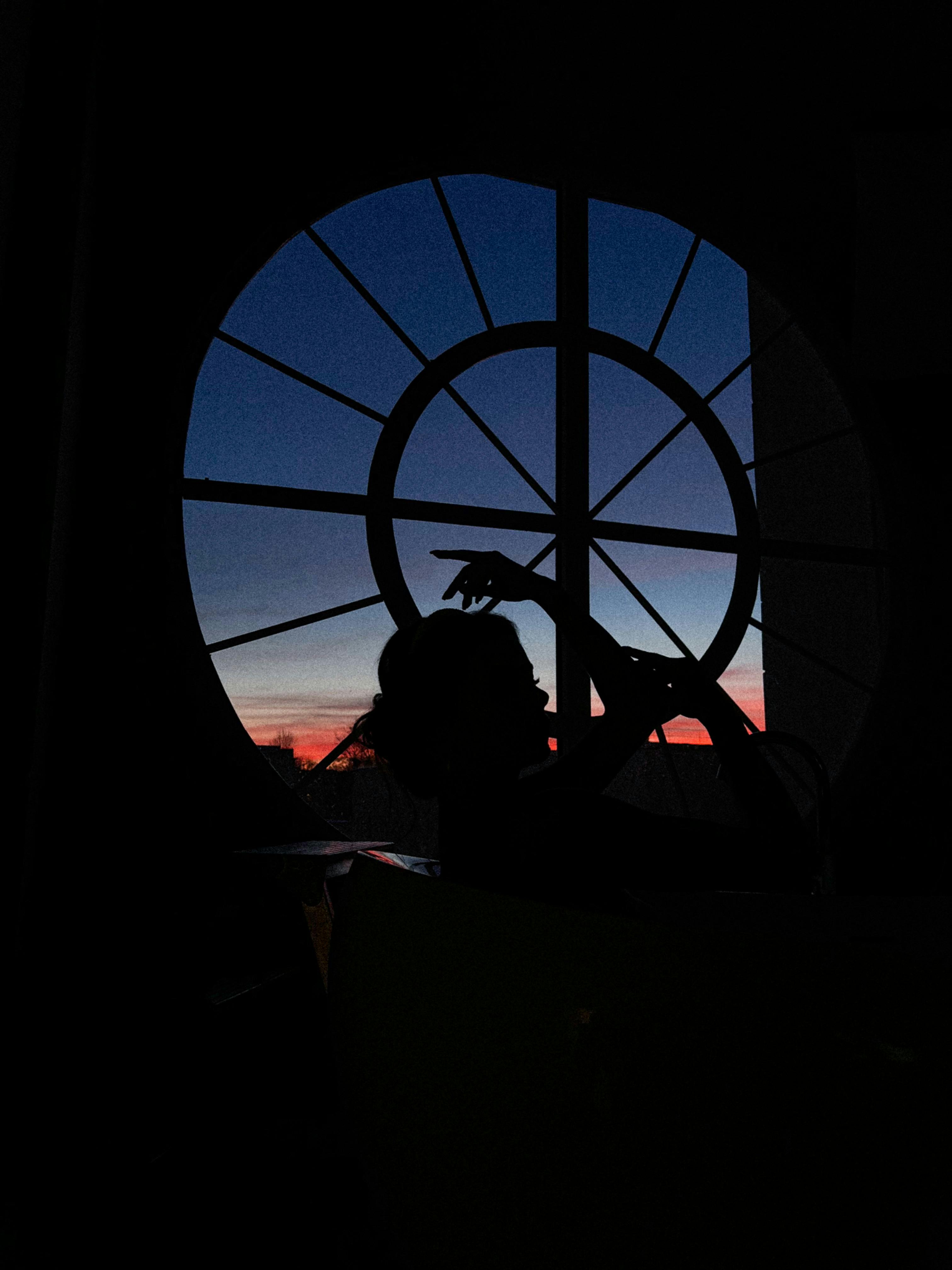 A silhouette of a woman posing gracefully by a circular window during a vibrant twilight in Minsk, Belarus.