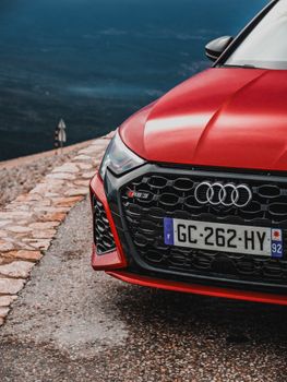 Front view of a red sports car parked on a scenic mountain road overlooking the ocean.