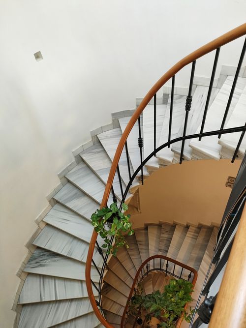 Free Top view of a spiral marble staircase with iron railings and plants enhancing its elegance. Stock Photo