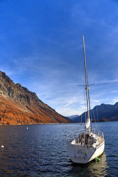 White sailing boat on a serene Italian lake with rocky mountain backdrop.