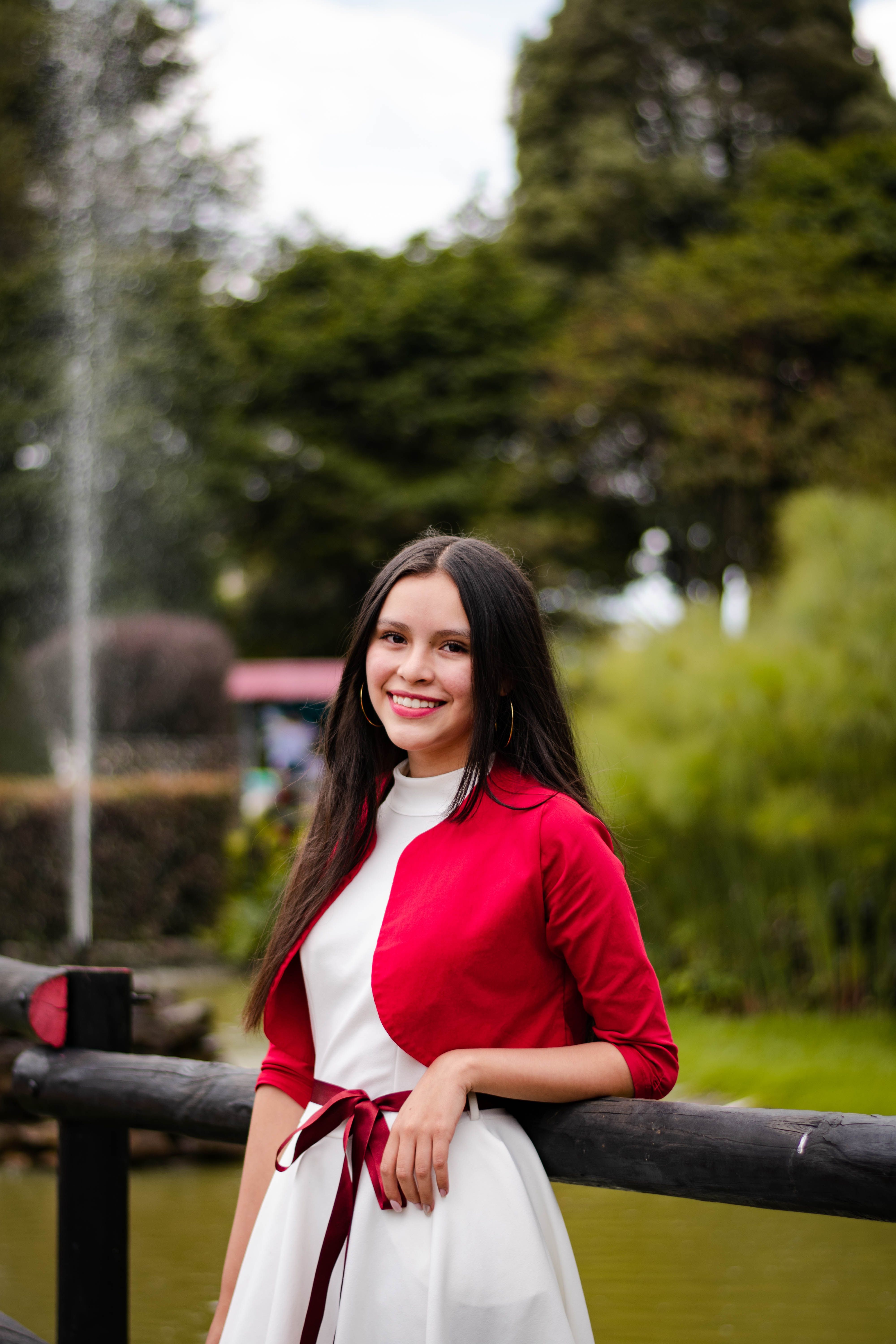 Cheerful woman posing in a red dress beside a fountain in a park.