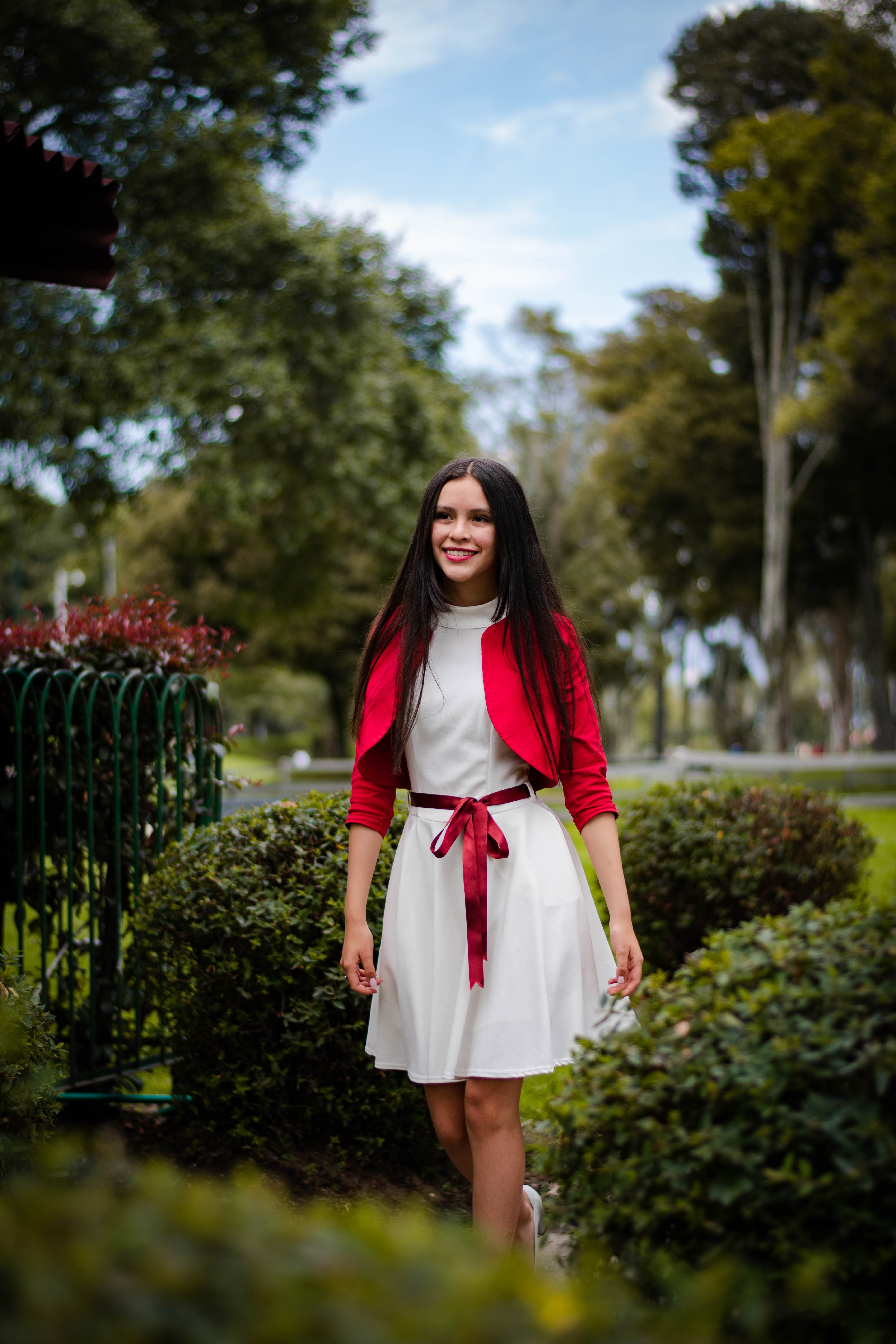 A Woman in Red Blazer and White Dress Standing Near Green Plants  Free  Stock Photo