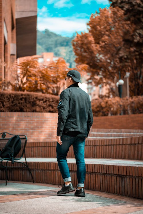 Free Man in Black Jacket and Blue Denim Jeans Walking on Concrete Pavement Stock Photo