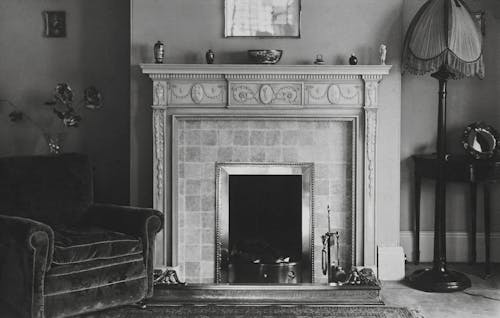 Grayscale Photo of an Armchair near a Fireplace