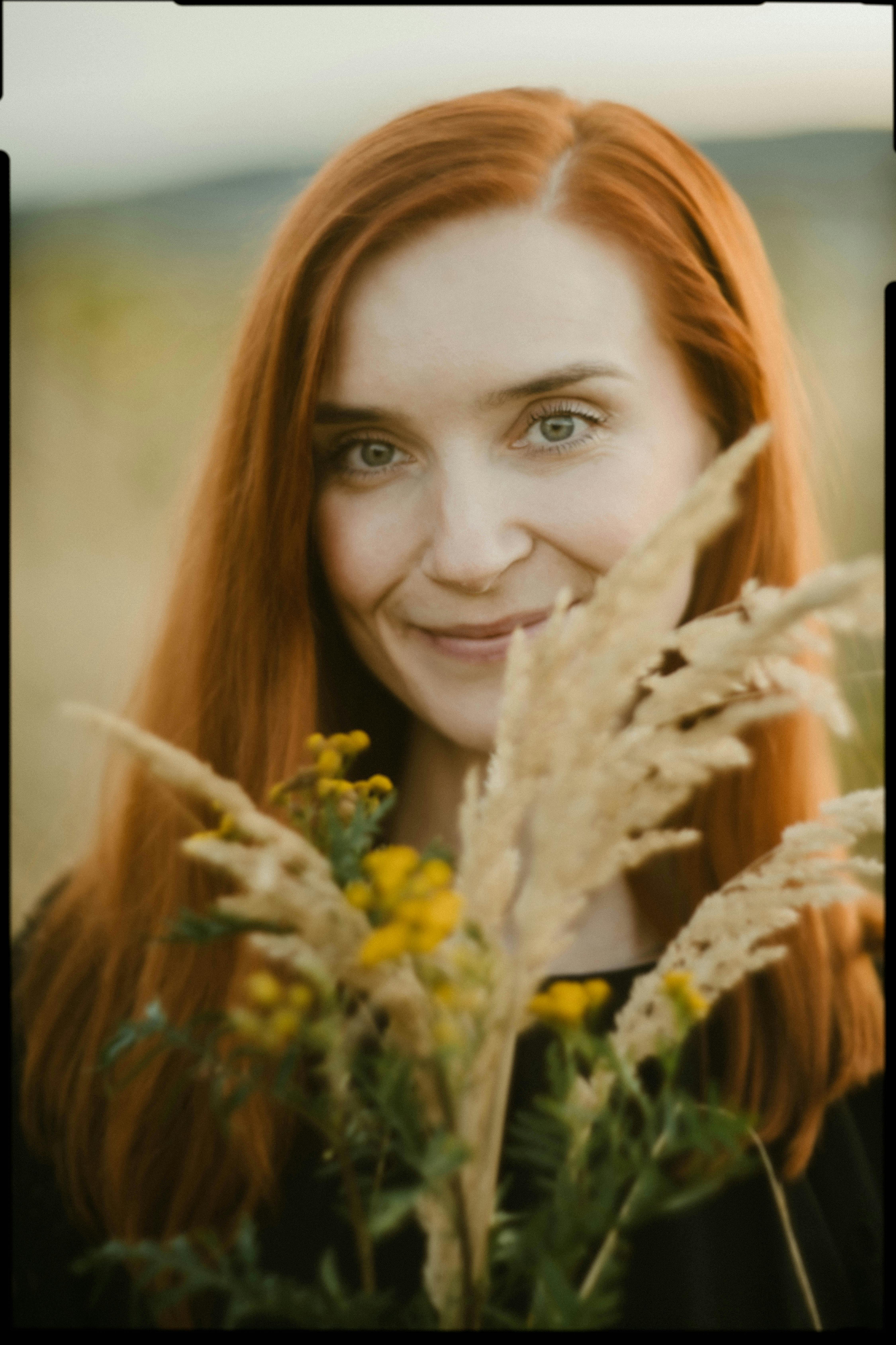 Portrait of a smiling woman with red hair holding wildflowers outdoors.