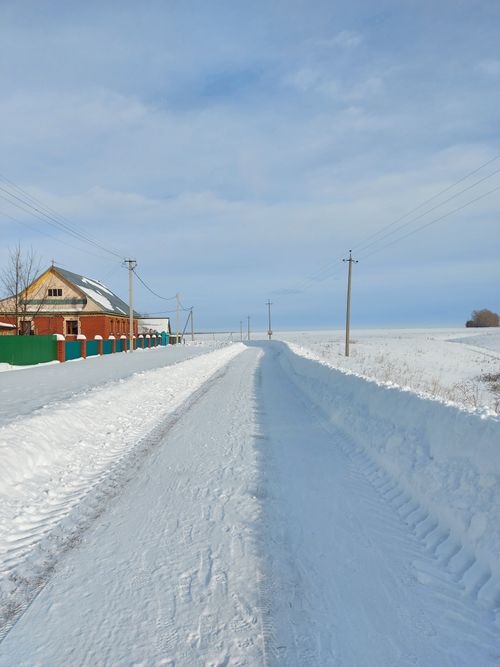 Free Rural winter scene with snow-covered road, house, and clear sky. Stock Photo