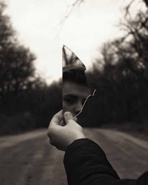 A Grayscale Photo of Person Holding a Mirror