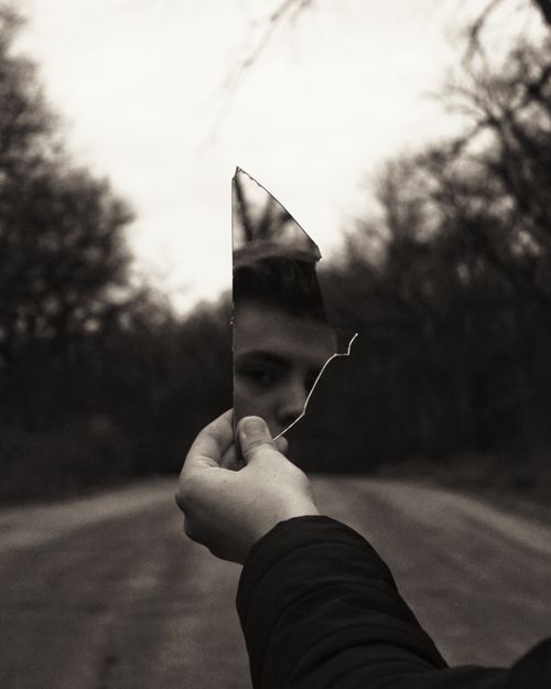 Free A thought-provoking black and white image of a man looking into a broken mirror. Stock Photo