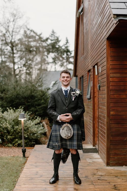 Free Smiling man in traditional Scottish kilt standing outdoors next to a wooden house. Stock Photo