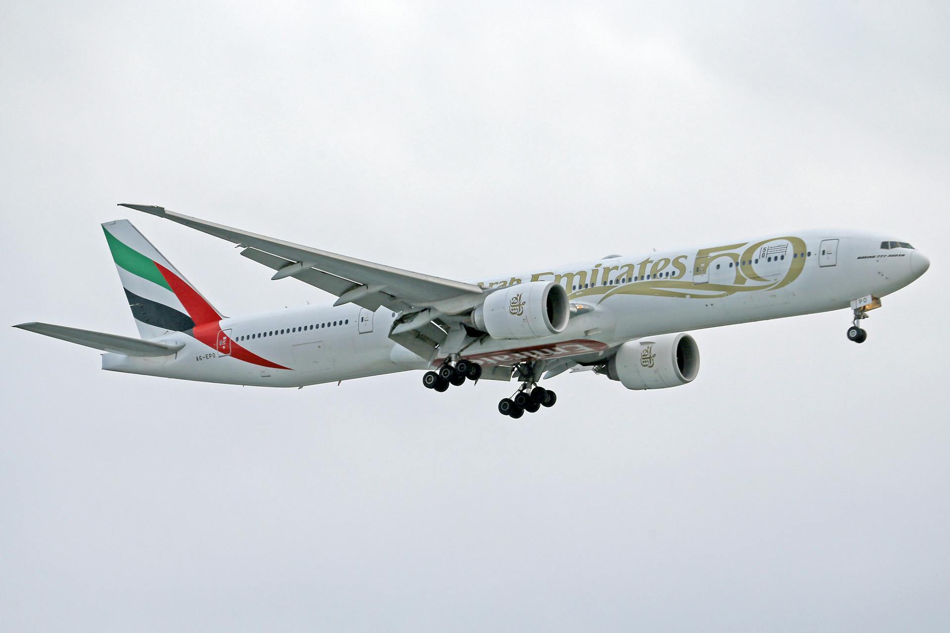 Boeing 777 in Emirates livery soaring amidst clouds, showcasing aviation elegance.