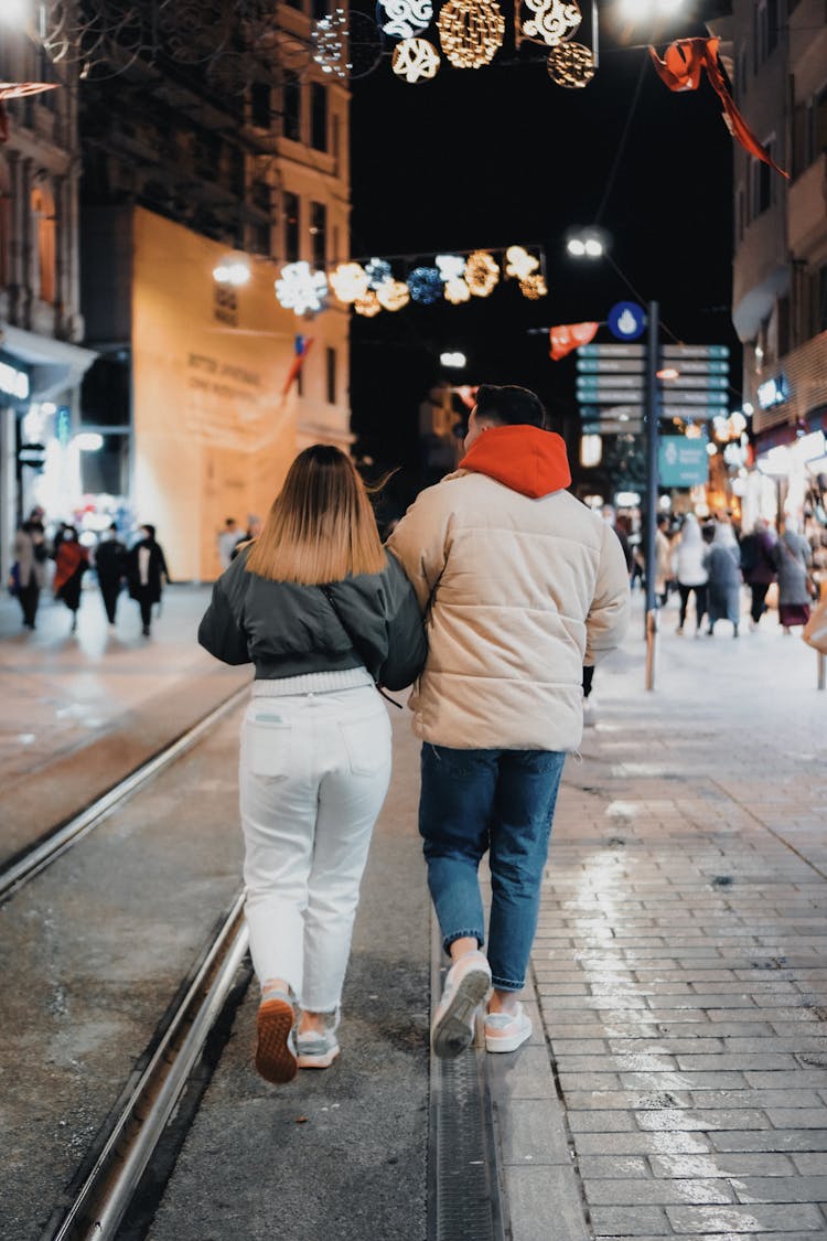 Couple In Winter Jackets Walking On Railway On Downtown