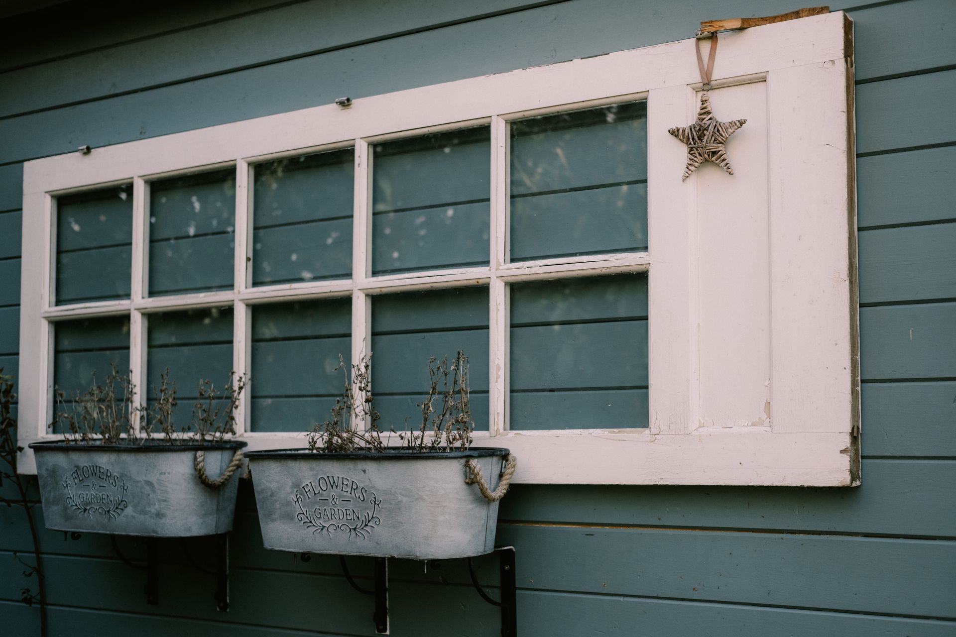 Charming rustic window frame with planters and star decor on a painted wooden exterior wall.