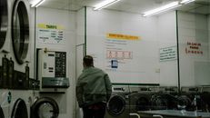 Man using a modern laundromat with washing machines and instruction signs.