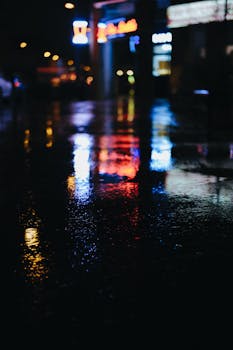 Blurred neon lights reflecting on wet city street at night, creating vibrant atmosphere.