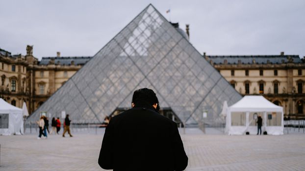 Man standing at the famous Louvre Pyramid in Paris, showcasing a classic tourist attraction.