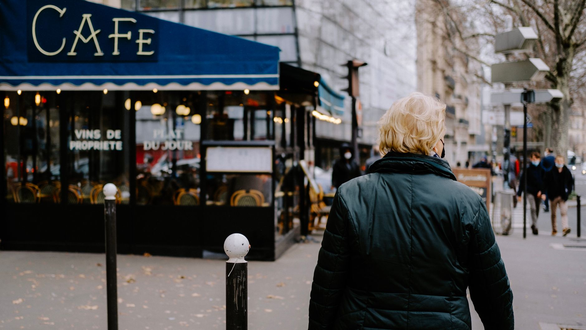 Person walking on a city street near a classic Parisian café under a blue awning.