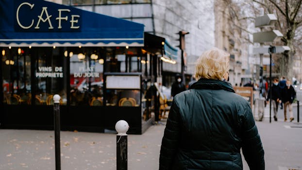 Person walking on a city street near a classic Parisian café under a blue awning.