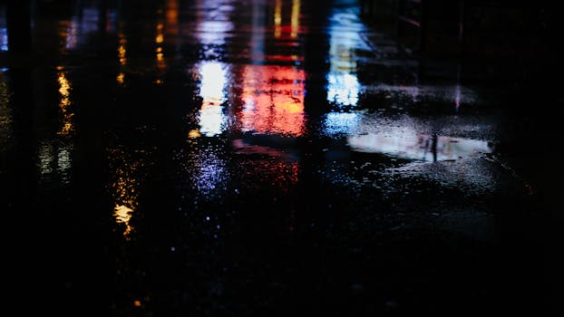 Colorful reflections of city lights on a wet street at night create a vivid, moody atmosphere.
