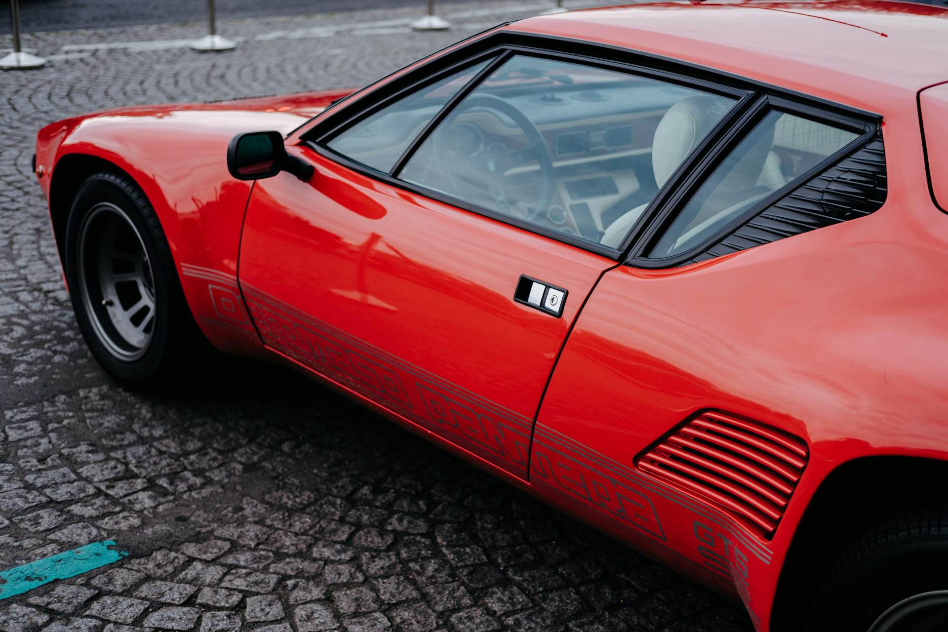 Detailed side view of a vintage red De Tomaso Pantera sports car on cobblestone street.