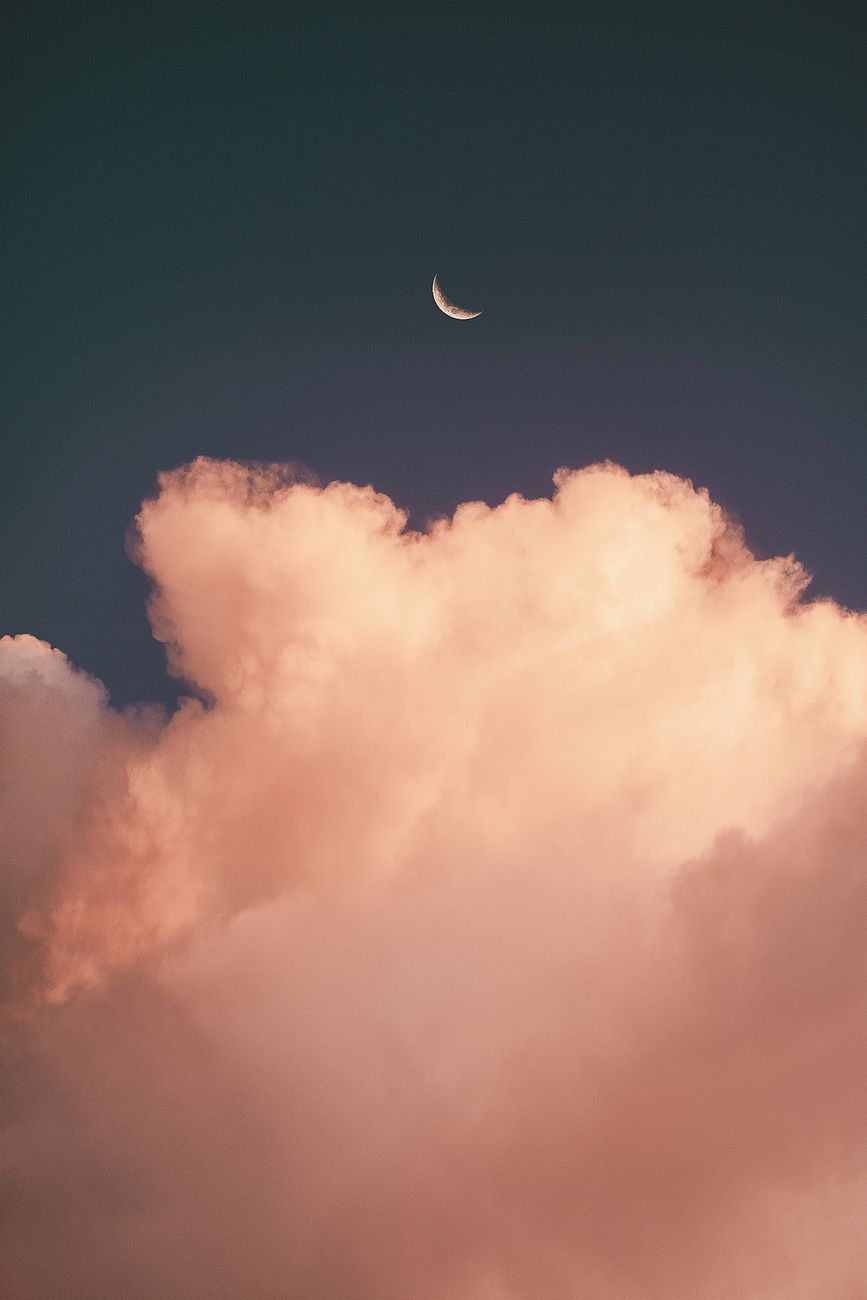 Stunning crescent moon captured over vibrant clouds during sunset in Brasília, Brazil.