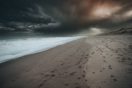 A moody beach scene with dramatic dark clouds, waves, and deserted sandy shore.