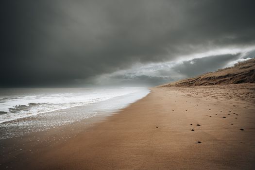 A serene sandy beach under dark, dramatic clouds, creating a moody coastal scene.