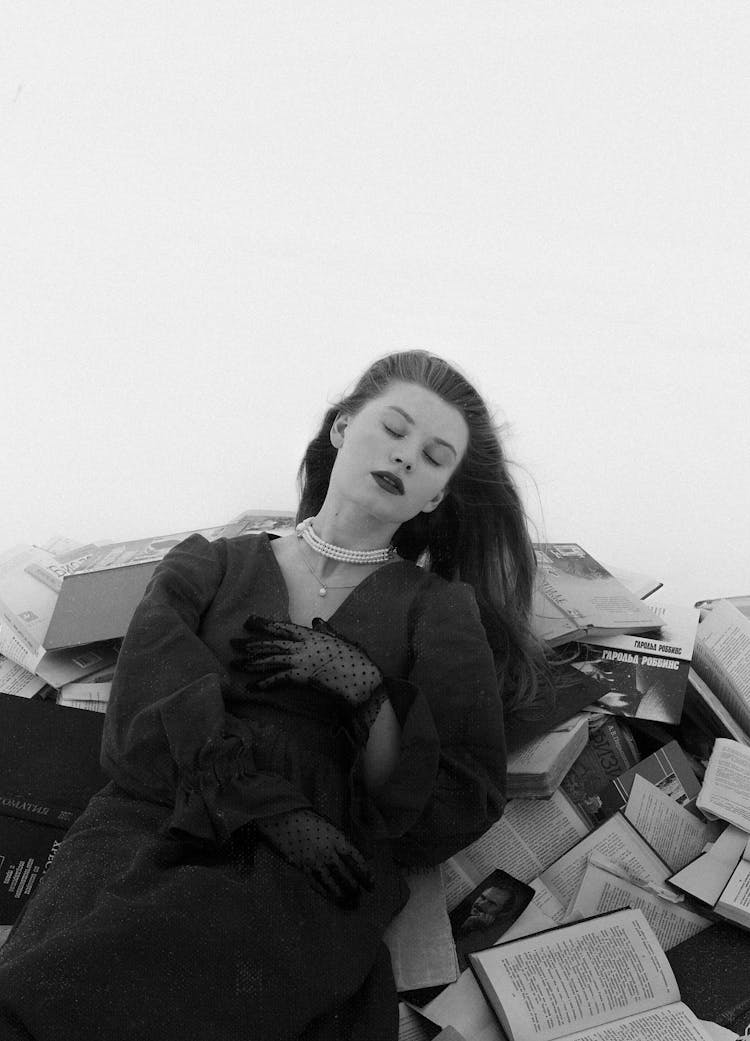 Young Woman In Dress Wearing Lace Gloves Leaning Against Pile Of Books