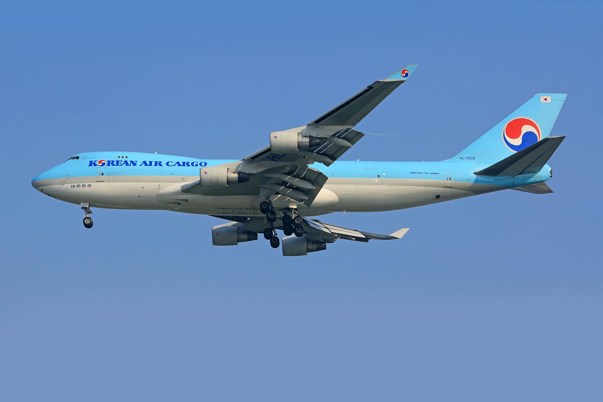 A Korean Air Cargo airplane flying in the clear blue sky, featuring a white and blue design.