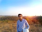 日落时分，一名穿着随意的年轻人站在印度的田野上