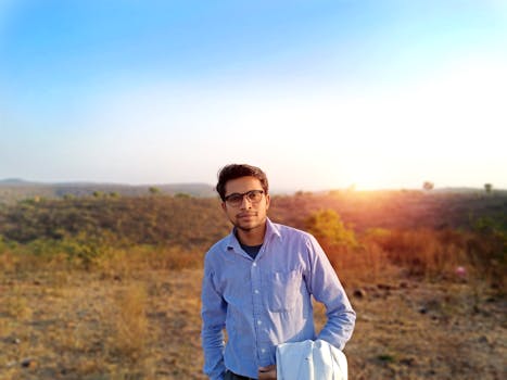 日落时分，一名穿着随意的年轻人站在印度的田野上