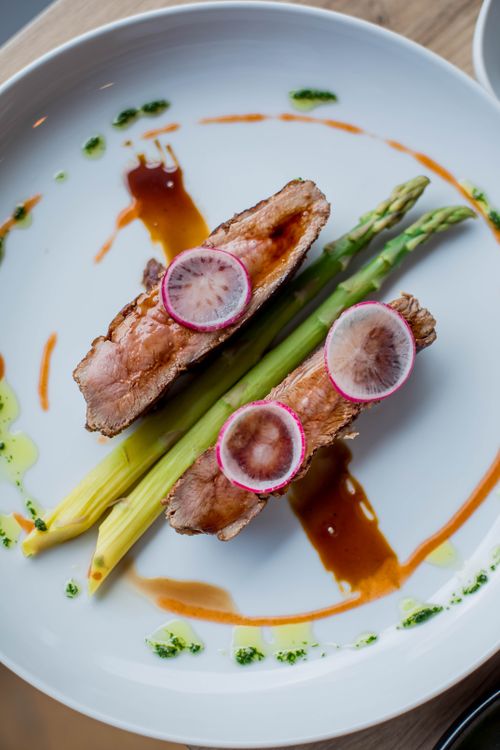 Free Deliciously plated gourmet meal featuring grilled meat and fresh asparagus with colorful garnishes. Stock Photo