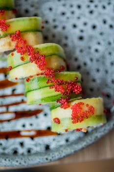 Artistic close-up of a cucumber sushi roll garnished with vibrant red caviar.