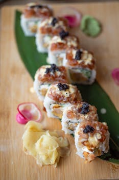 Appetizing sushi roll topped with caviar, served on a wooden board with ginger and wasabi.