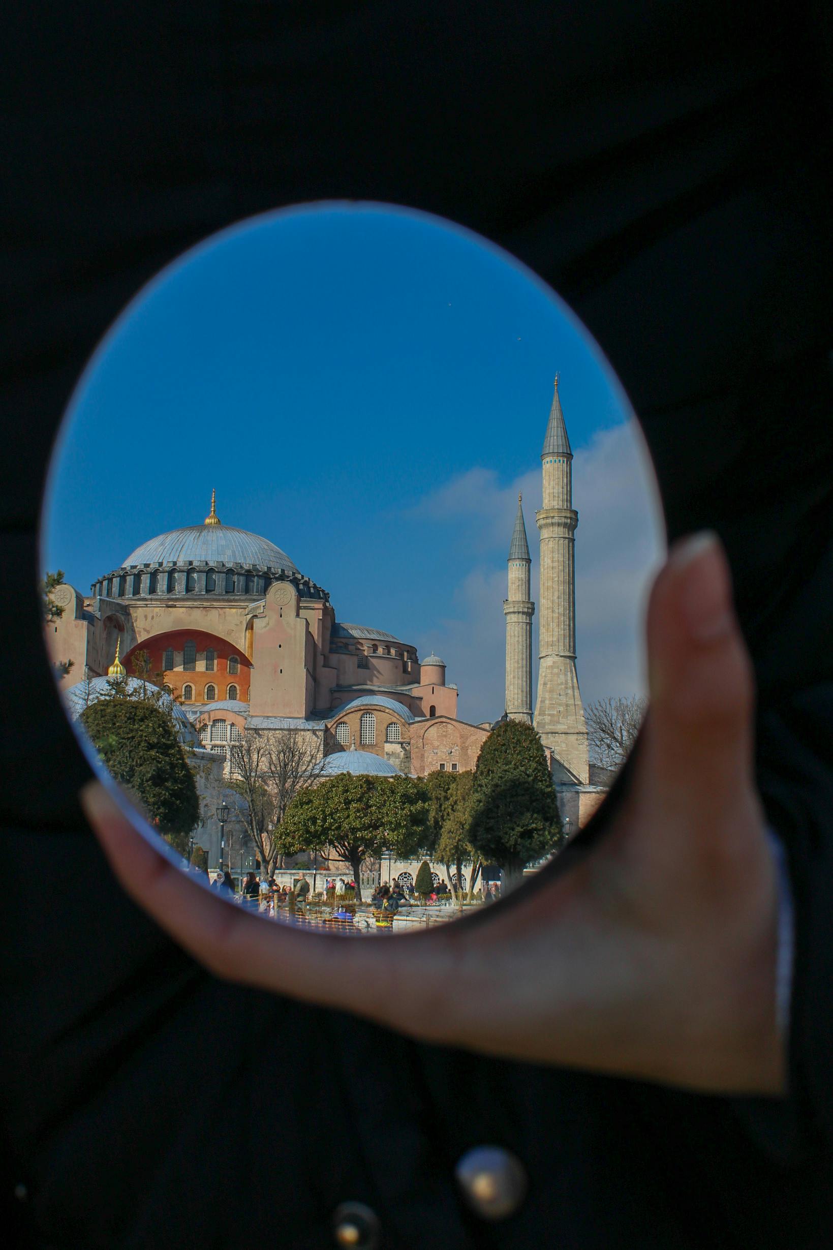 An artistic reflection of Hagia Sophia captured in a handheld mirror against a clear blue sky.
