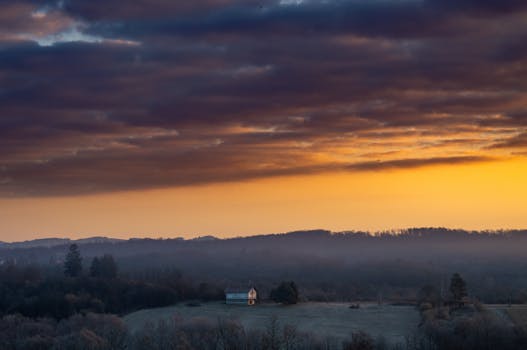 Captivating rural landscape at sunset with a house silhouetted against the orange sky.