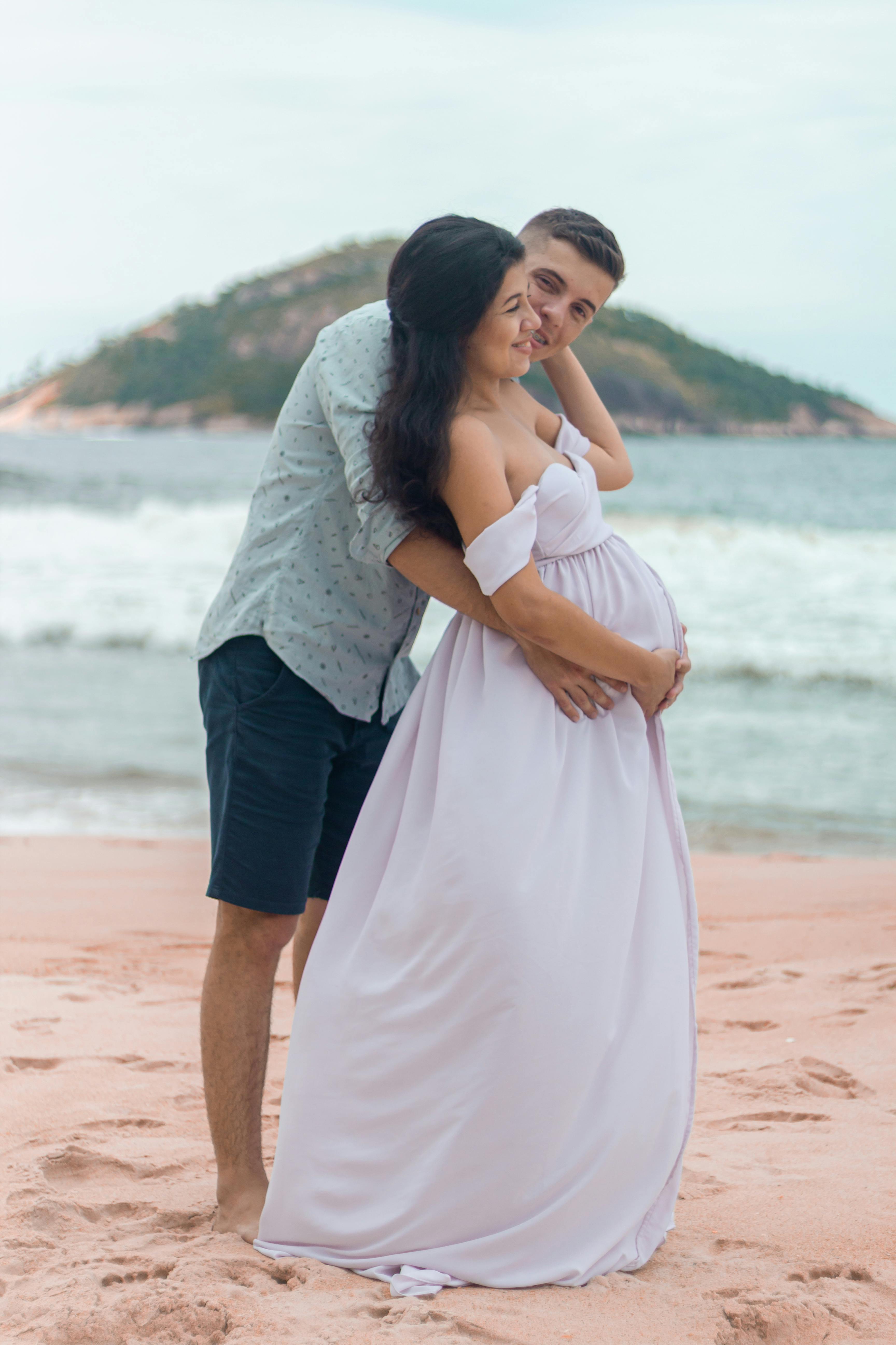 a husband embraces pregnant wife on the beach