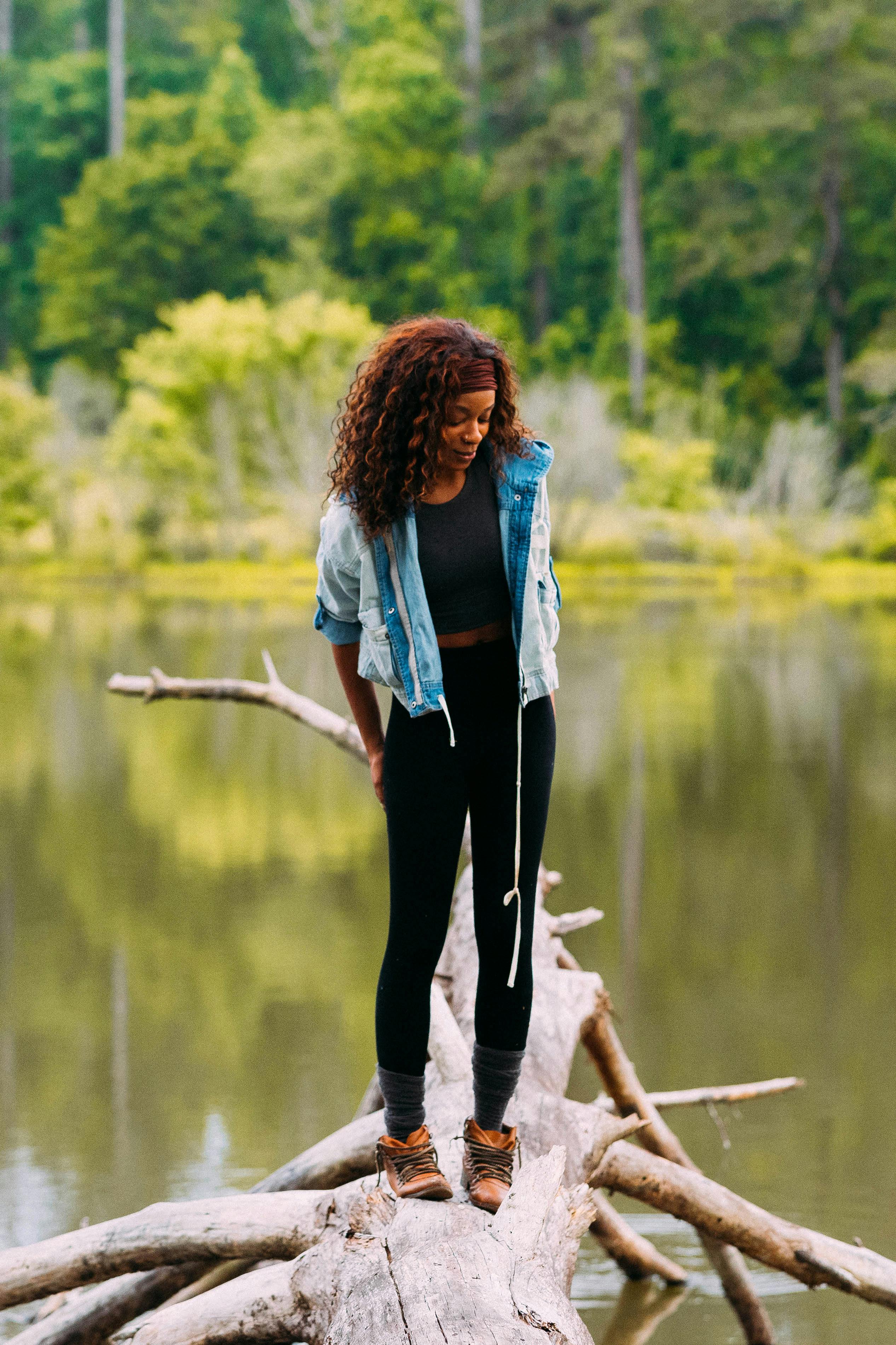 a woman in blue denim jacket and black pants standing on brown wooden log